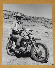 a man riding on the back of a motorcycle down a dirt road next to a hill