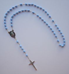 "Guardian Angel Blue Rosary with Pouch Included. Made in Italy This is one of the best rosaries you can buy...made to last a long time. It can also be used as a necklace rosary. This listing includes (1) rosary. Blue beads with detailed silver tone Crucifix 1-3/4\" long. SIZE/LENGTH: Total length is 18\" including the Crucifix. BEADS: Quality blue oval beads measure 1/4\" x 3/16\" (7mm x 5mm) carefully assembled on a zinc alloy chain. CENTER PIECE:  Zinc alloy center piece of The Guardian Angel Adjustable Blue Rosary With Miraculous Medal, Blue Cross Rosary For Gift, Blue Cross Rosary As Gift, Blue Crib, Blue Rosary, Pink Crib, Angel Blue, Oval Beads, Guardian Angel