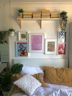 a bed with pillows and pictures on the wall above it in a room that is decorated with potted plants