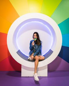 a woman sitting in front of a rainbow colored wall