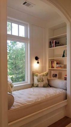 a window seat in the corner of a room with bookshelves and pillows on it