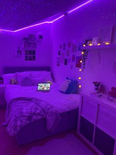 a bed room with a laptop computer on it's side and purple lights hanging from the ceiling