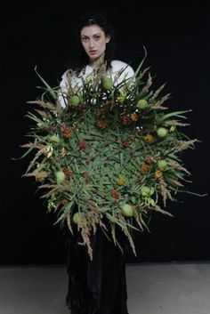 a woman standing in front of a black background holding a bouquet of flowers and fruit