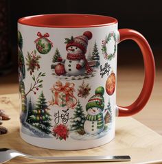 a red and white coffee mug with christmas decorations on it next to a spoon and fork