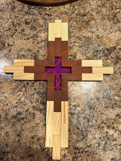 a cross made out of wood with red circles on the center and purple fabric around it