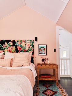 a bedroom with pink walls and floral headboard, rugs on the floor and bed