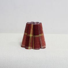 a red and yellow plaid vase sitting on top of a white cloth covered tablecloth