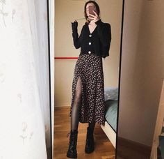 a woman taking a selfie in front of a mirror wearing black boots and a floral print skirt