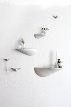 three white shelves on the wall with plants and candles in them, hanging from hooks