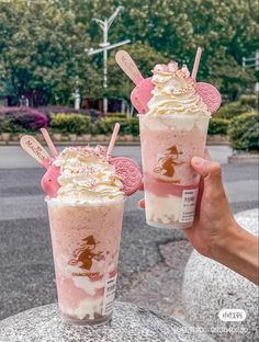 two people holding up drinks with straws in their hands, one is strawberry milkshake and the other has whipped cream