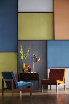 two chairs and a table in front of a wall with different colored panels on it