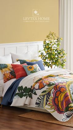 a bed with colorful comforters and pillows in a room next to a potted plant