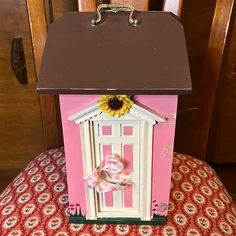 a pink and brown dollhouse with a sunflower on the front door is sitting on a chair