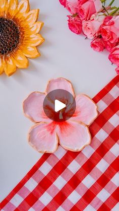 a red and white checkered table cloth with flowers on it next to a candle