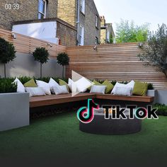 an outdoor seating area with wooden slats and green cushions on the grass in front of a brick building