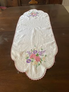 an old table cloth with flowers on it sitting on top of a wooden table next to a drawer