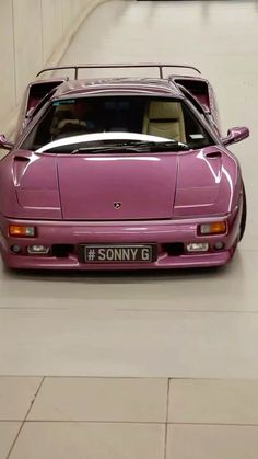 a pink sports car parked in a parking garage next to a white wall and tiled floor