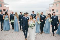 a bride and groom walking with their bridal party in front of the beachfront