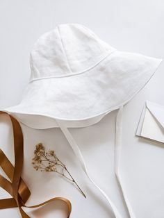 a white hat sitting on top of a table next to a brown ribbon and some flowers