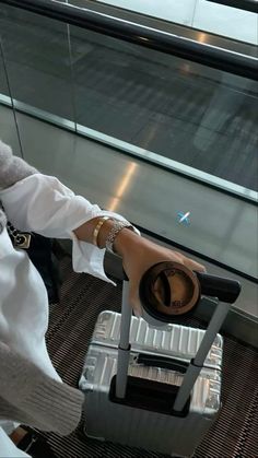 a woman sitting on top of a luggage bag next to an airport window with her arm in the air