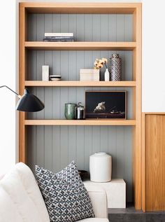 a white couch sitting in front of a wooden shelf filled with books and vases