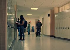 several people are walking down the hallway in a building with lockers on both sides