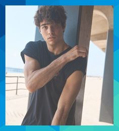 a young man leaning against a wall on the beach