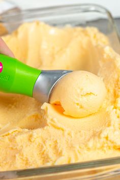 a person scooping ice cream into a bowl with a green plastic spoon in it