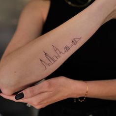 a woman's arm with a city skyline tattoo on the left side of her arm