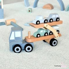 a wooden toy truck carrying cars on it's back in the middle of a play area