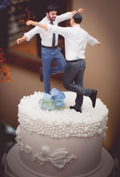 two figurines are posed on top of a wedding cake, one is jumping and the other is dancing