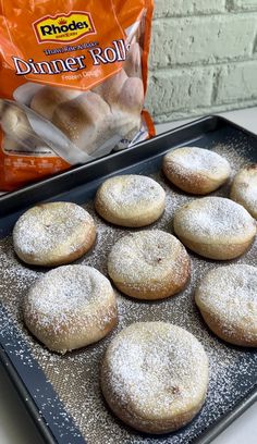 powdered sugar covered donuts are on a baking tray next to a bag of dinner rolls