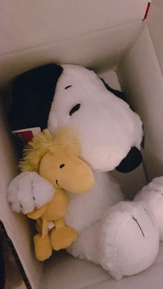 a white stuffed dog in a box with its head on a yellow teddy bear's paw