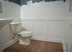 a white toilet sitting in a bathroom next to a wall mounted sink and wooden floors