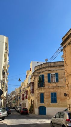 cars are parked on the street in front of buildings with blue shutters and balconies