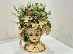 a ceramic head with flowers and plants on it's face is shown in front of a white wall