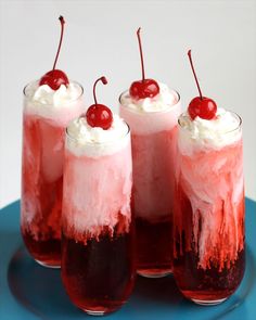 three glasses filled with ice cream and cherries on top of a blue tablecloth