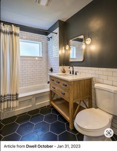 a white toilet sitting next to a bath tub under a bathroom mirror on top of a wooden cabinet