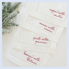 three embroidered napkins with words written on them next to a small pine tree branch