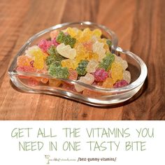 a heart shaped container filled with gummy bears on top of a wooden table next to a sign that says get all the vitamins you need in one tastyy bite