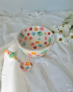 a bowl and spoon sitting on top of a white table cloth next to daisies