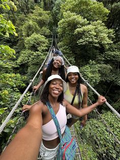 three women standing on a suspension bridge in the forest, smiling and taking a selfie