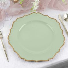 a green plate with gold trim sits on a white table cloth next to silverware