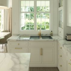 a white kitchen with marble counter tops and gold faucet pulls on the cabinet doors