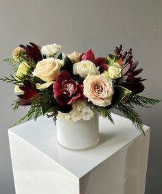 a white vase filled with lots of flowers on top of a white cubed table