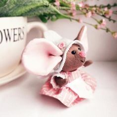 a small stuffed animal in a pink dress next to a coffee cup with flowers on it