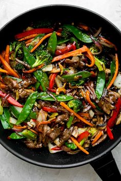 stir fry with vegetables and meat in a skillet on a white table top, ready to be eaten