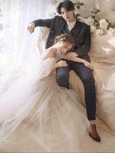 a man and woman sitting on a couch in front of a window with white flowers