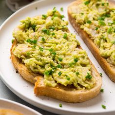 two pieces of bread with avocado on them are sitting on a white plate