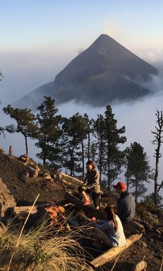 two people sitting on a bench in front of a mountain with fog and low lying clouds